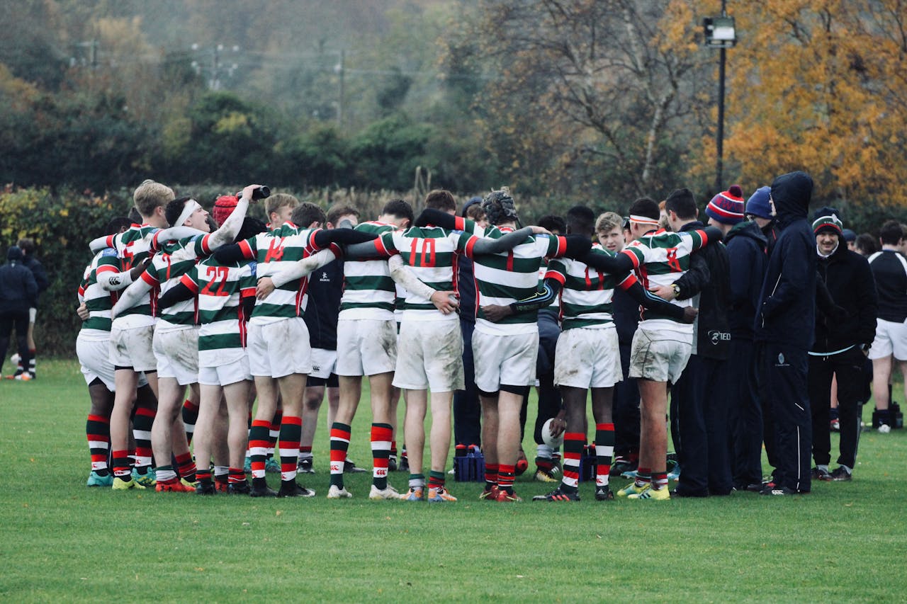 about-us Rugby players in striped jerseys huddle during a game on an autumn field.